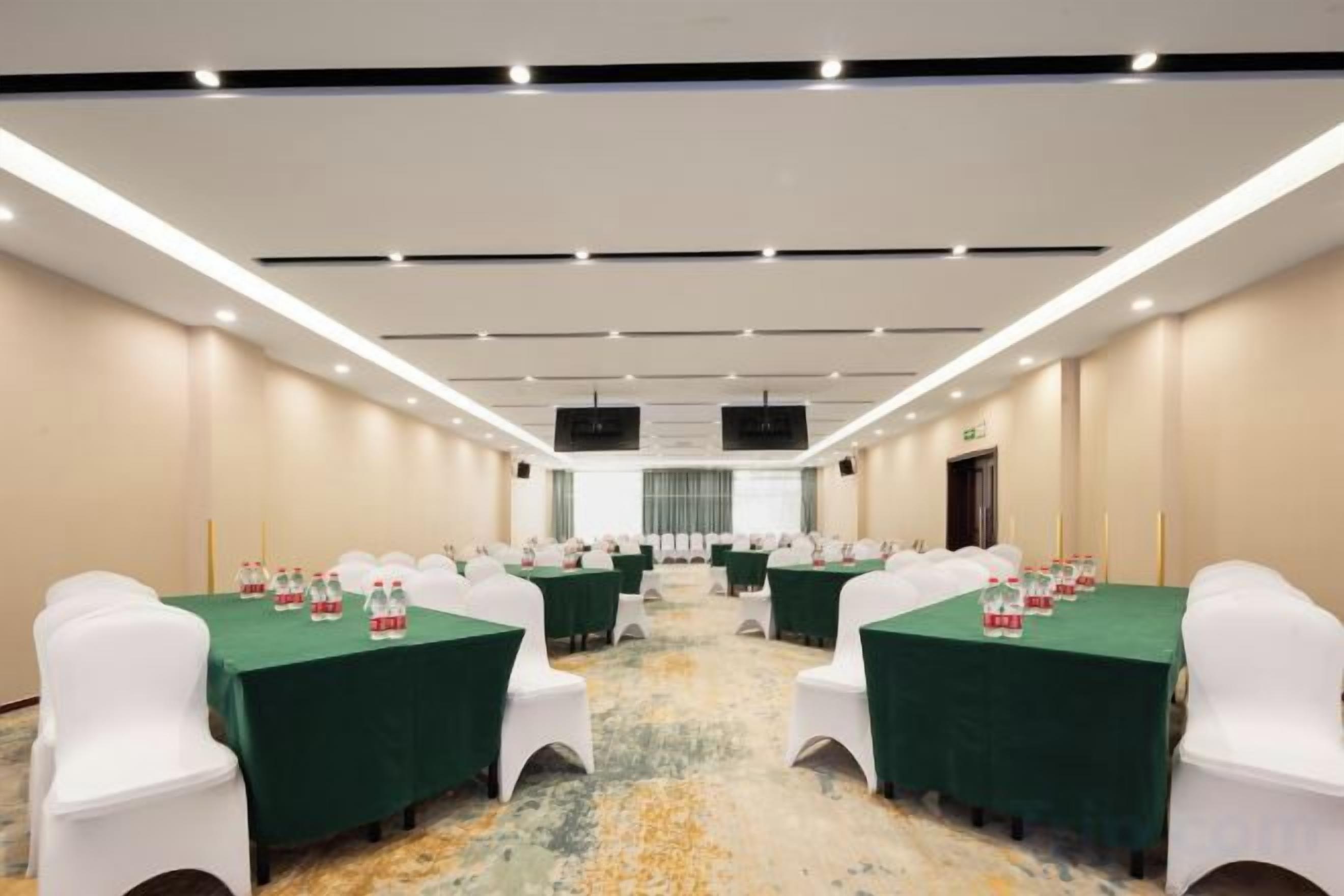 Une salle de conférence équipée de tables et de chaises, dotée d’un sol recouvert de moquette et d’une longue table recouverte d’une nappe verte.