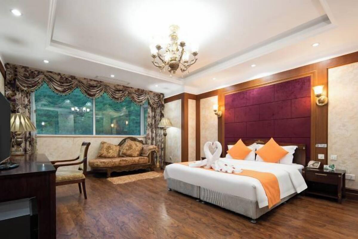 Une chambre d’hôtel avec un grand lit, un canapé, un bureau et un lustre.