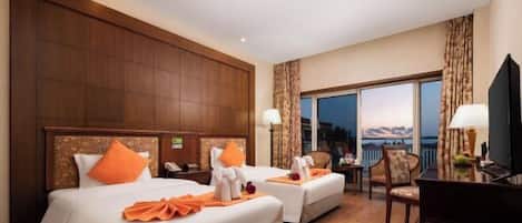 A hotel room with two beds, a desk, a chair, and a view of the outdoors.
