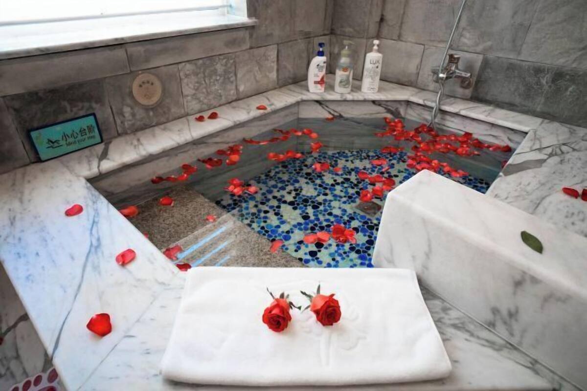 Une salle de bain avec une baignoire en marbre, des pétales de rose et des produits de toilette.