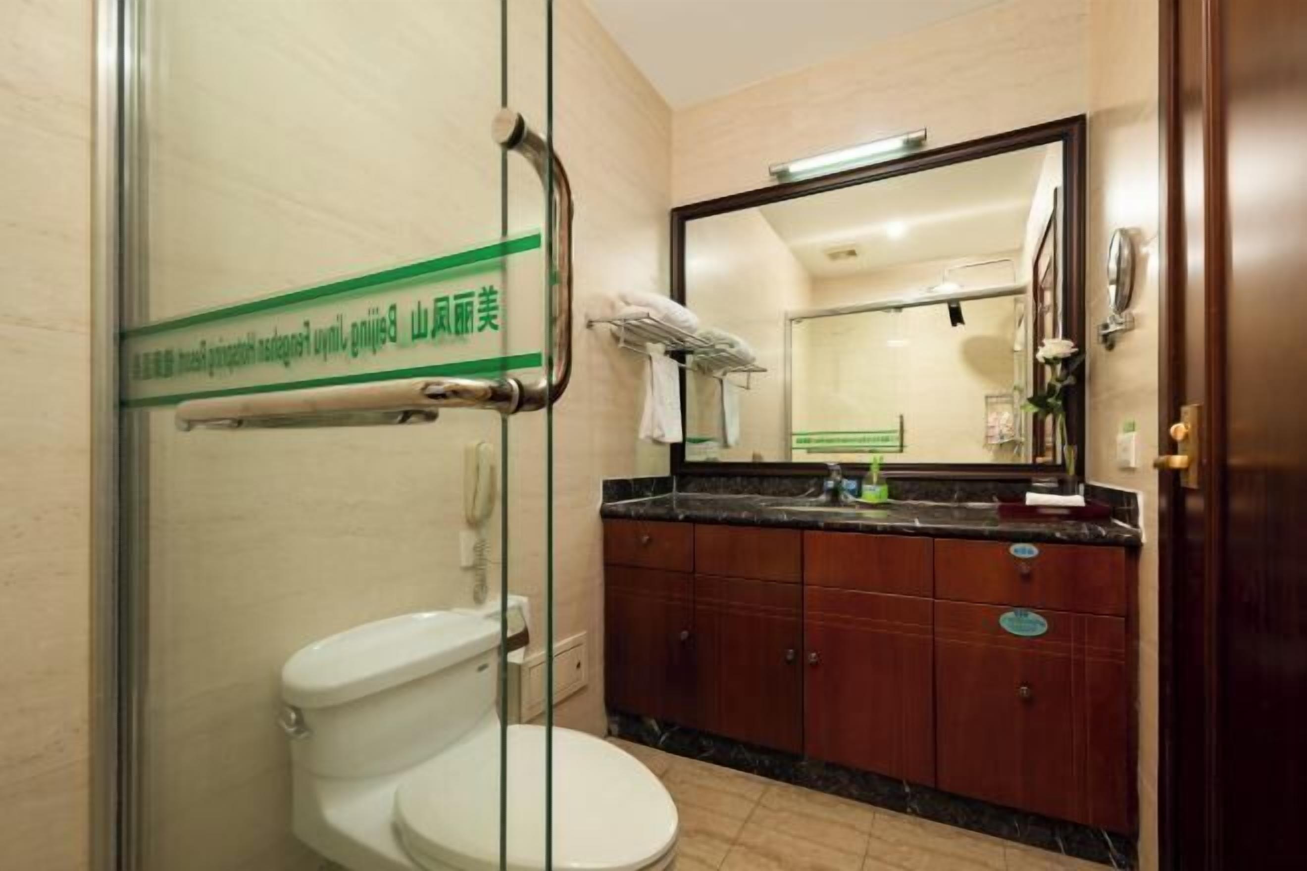 Un baño con inodoro, cabina de ducha de vidrio, tocador con espejo y un cartel en la pared.