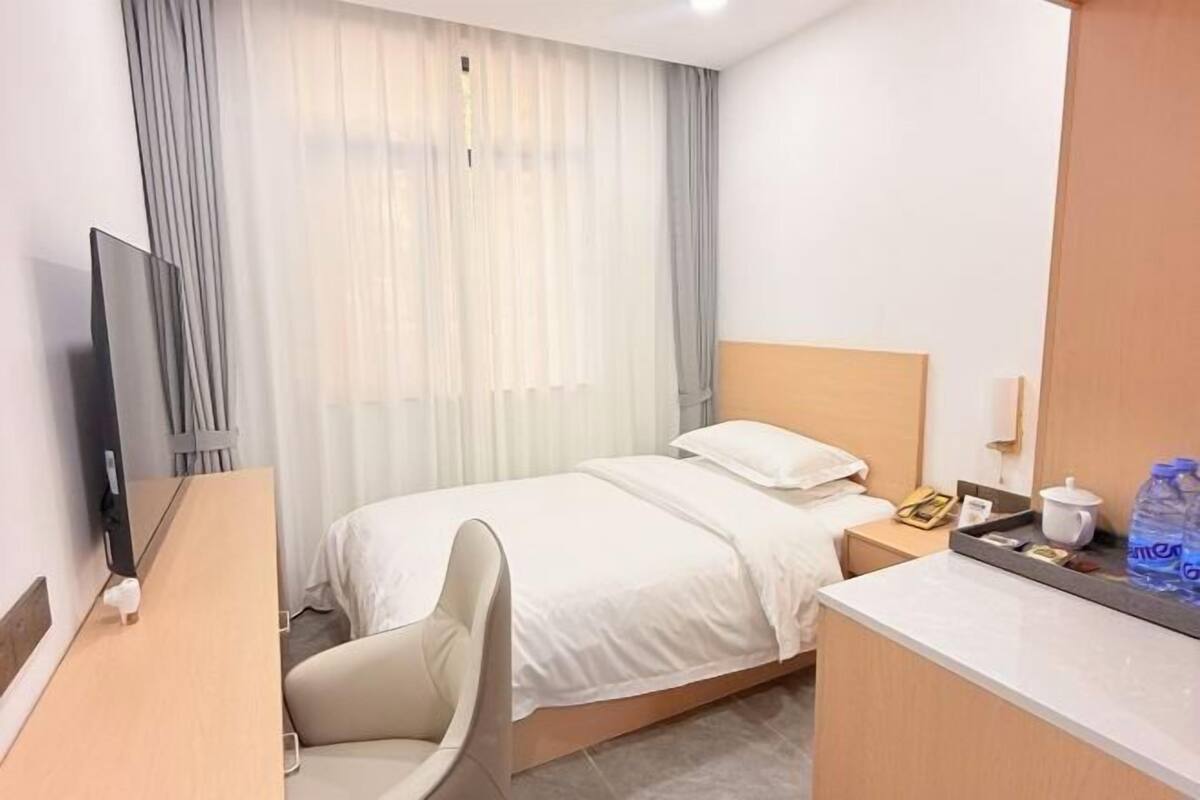 Une chambre d’hôtel comprenant un lit, un bureau, une chaise, une télévision, une table de chevet et une fenêtre avec des rideaux.