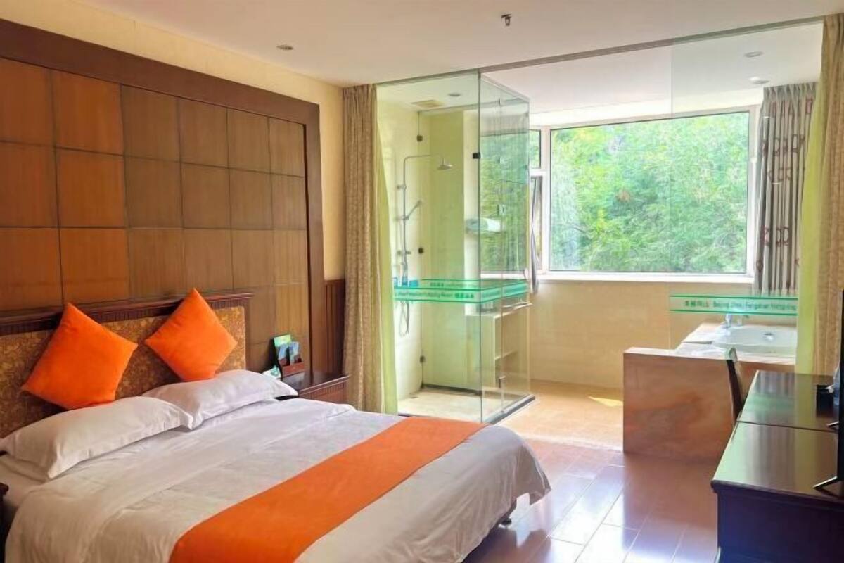 Une chambre d’hôtel avec un lit, une douche en verre, un bureau et une vue sur la verdure.