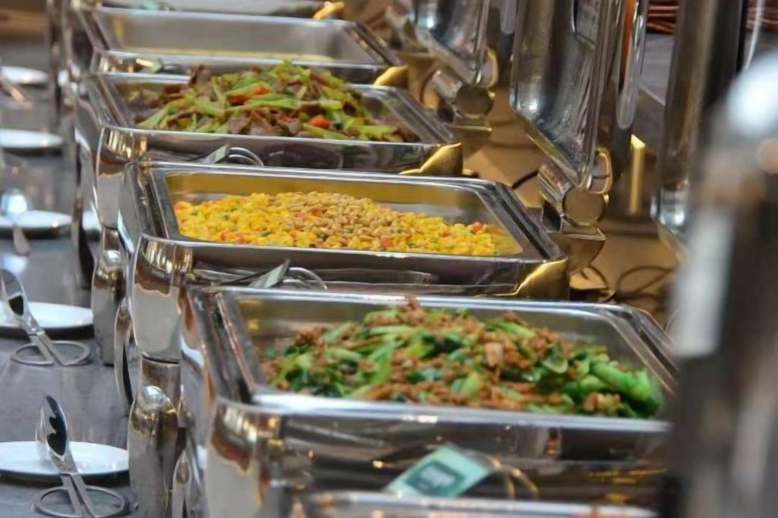 Un bufé con diversas opciones de comida en bandejas de metal.