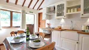 Un coin repas avec une table mise pour le repas, une cuisine avec des meubles blancs et un fourneau, et une fenêtre avec des rideaux.