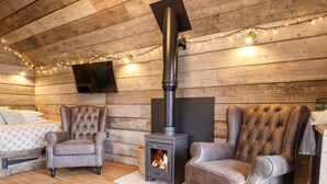 A cozy room with a wood-burning stove, two leather armchairs, a bed with a polka dot duvet, and a flat-screen TV mounted on the wall. - Sunset Retreat (Scarborough)