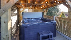 A hot tub under a wooden pergola with string lights, surrounded by a wooden fence and trees in the background. - Sunset Retreat (Scarborough)