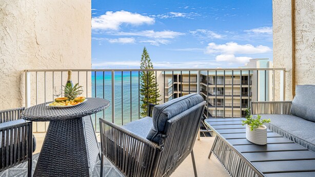 A balcony with wicker furniture, a potted plant, and a plate of fruit. - Ocean Tropics Oasis, Beachfront, King bed, AC/pool (Lahaina)