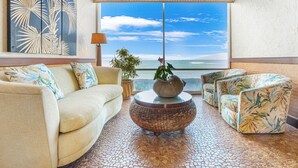 A living room with a sofa, armchairs, a coffee table, and a large window with a view of the ocean. - Ocean Tropics Oasis, Beachfront, King bed, AC/pool (Lahaina)