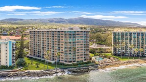 A high-rise hotel with multiple balconies, a pool area, and a view of the ocean and mountains. - Ocean Tropics Oasis, Beachfront, King bed, AC/pool (Lahaina)