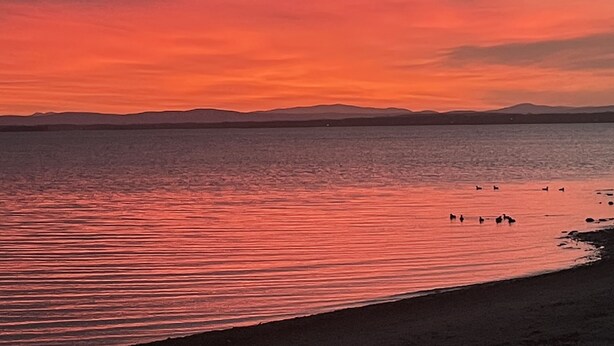 A sunset over a calm body of water with silhouettes of mountains in the background.