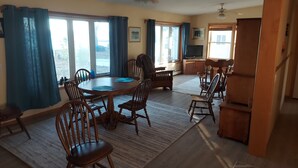 A spacious living room with a dining area, large windows, and a ceiling fan.
