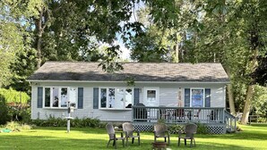 A white house with a porch, surrounded by a grassy yard and trees.