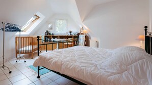A bedroom with a large bed, a crib, a desk with a chair, and a window with a view of trees. - Carnac - 4-room house - 102m² - Wifi - 2* (CARNAC)