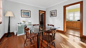 A dining area with a glass-top table, wooden chairs, a lamp, and artwork on the walls. - Carriage House: Perfect for Summer Explorations – Comfortable Loft Living (Wyandotte)