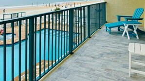 Ein Balkon mit Blick auf den Strand und den Ozean, ein Schwimmbecken und zwei blaue Adirondack-Stühle.