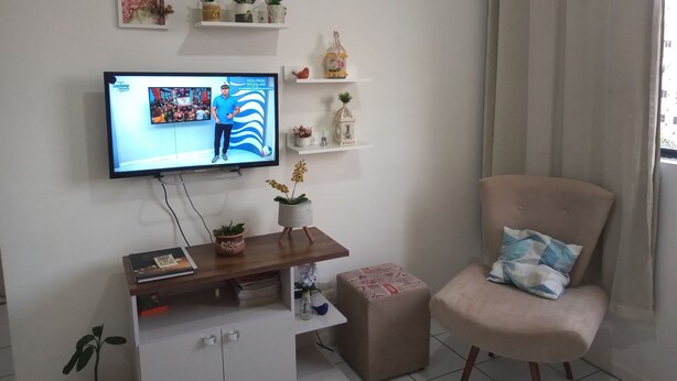 Un salón con televisor en la pared, un sofá, una mesa de centro y diversos objetos decorativos.