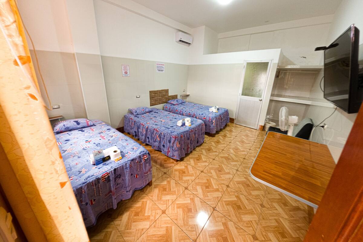 A room with three beds, a wooden desk, a television, and a mirror.