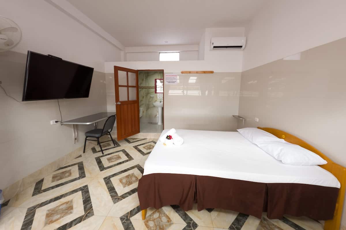A hotel room with a bed, a desk, a chair, a television, and an air conditioning unit.