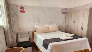 Une chambre d’hôtel avec un lit, une armoire en bois, un petit tabouret et un panneau indiquant qu’il est interdit de fumer.