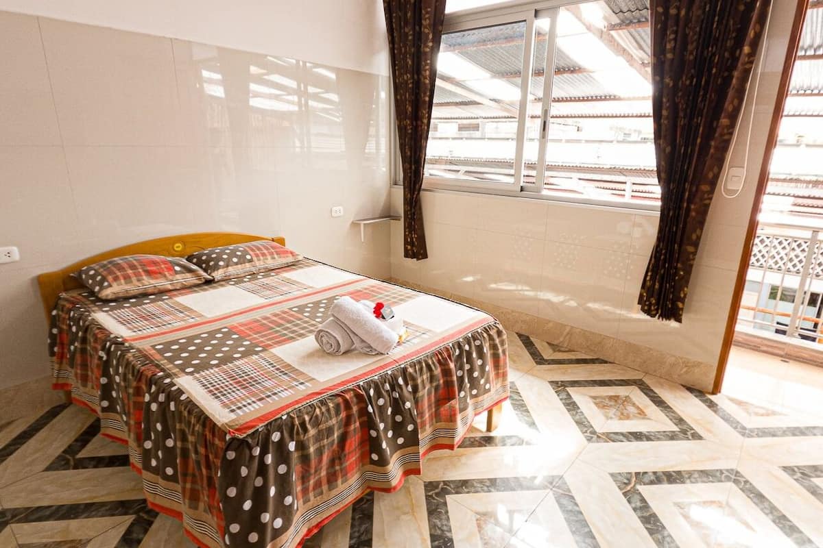 A bedroom with a bed, a window, and a view of buildings outside.