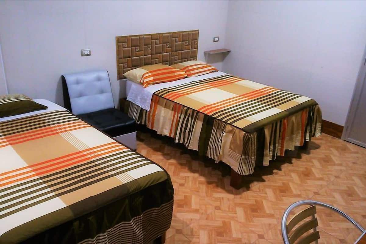 A hotel room with two single beds, a chair, and a small table.