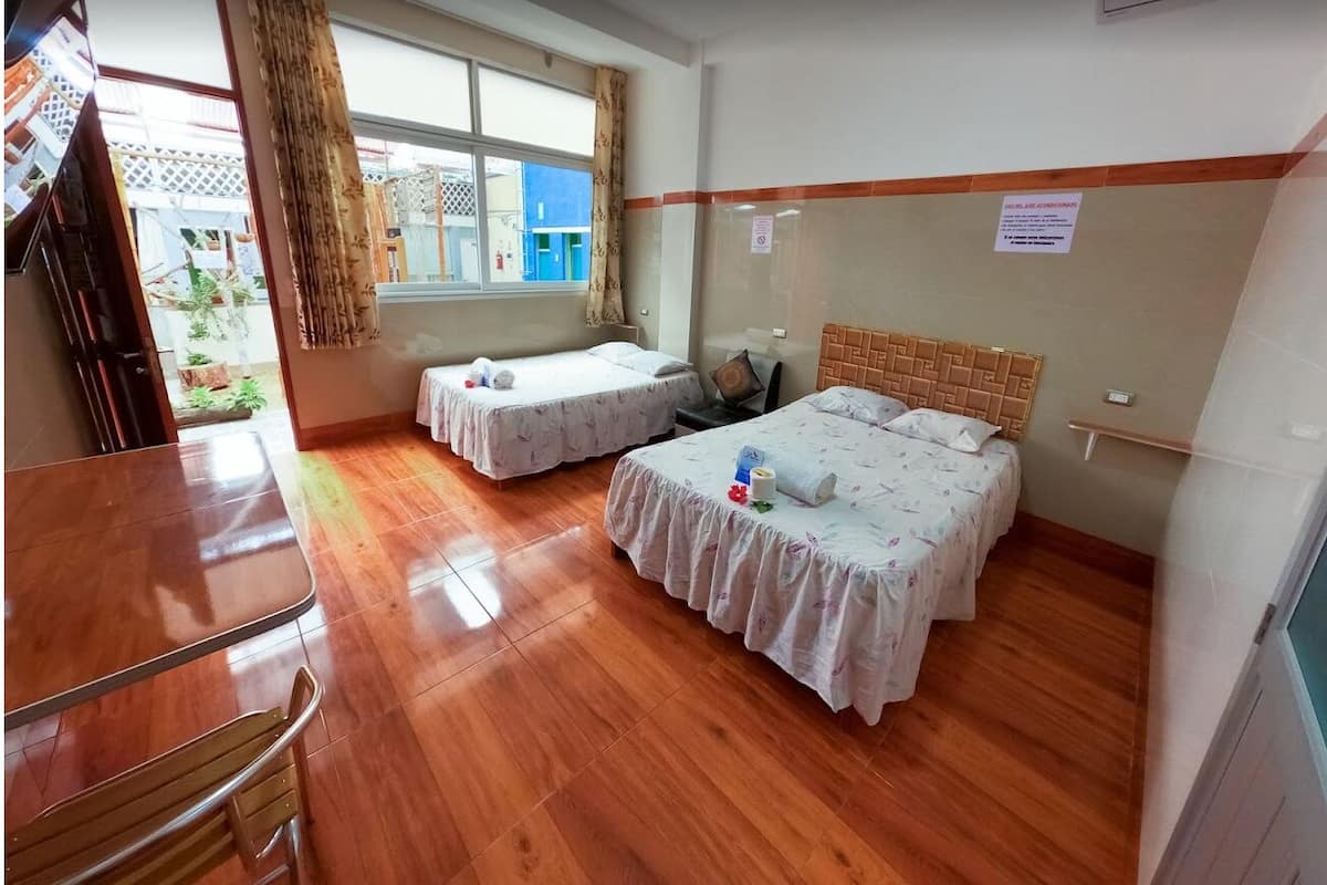 A room with two beds, a wooden floor, a window with curtains, and a small table.