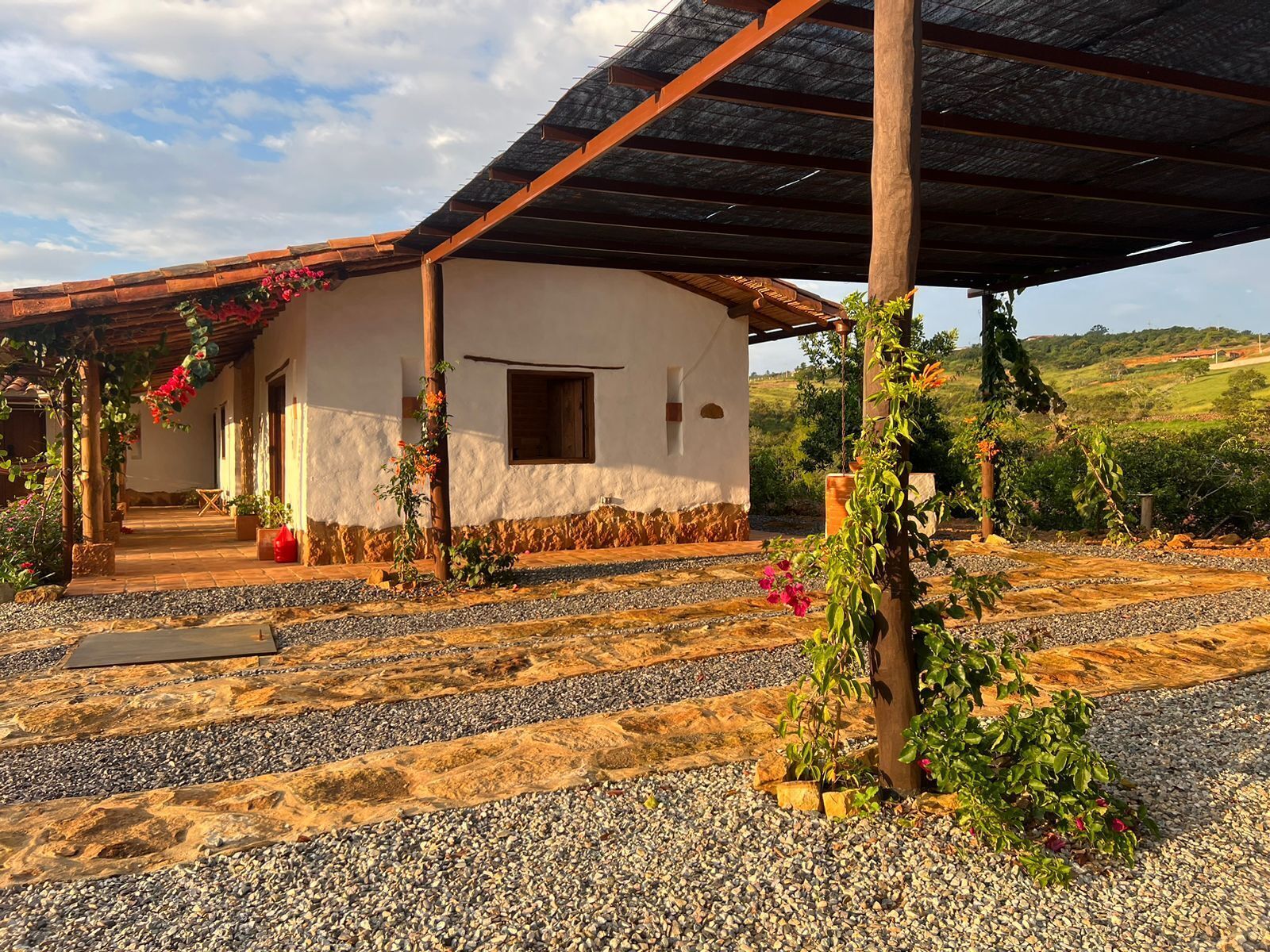 A rustic building with a tiled patio, a wooden pergola, and a gravel pathway leading to the entrance.