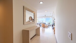 A modern interior with a reception desk, a large mirror with a woven frame, and a view of a living area with a sofa and a TV. - Península T3 1A Luxurious Ocean View Getaway! (Puerto Vallarta)