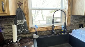 Una cocina con un ventanal amplio, armarios de madera, un lavamanos negro y un dispensador de toallas.