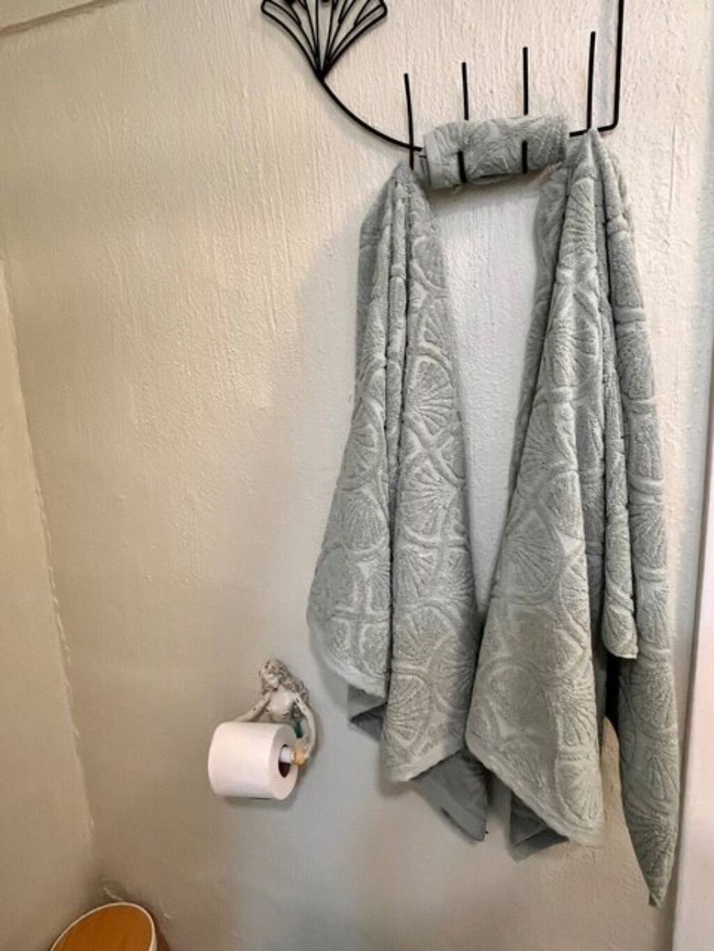Een badkamer met een handdoekrek met twee gestreepte handdoeken, een toiletpapierrol en een decoratief metalen object aan de muur.