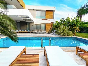 A modern poolside area with lounge chairs, a pool, and a contemporary building with large windows.