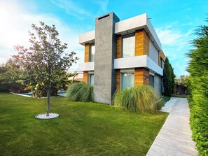 Uma casa moderna de dois andares com um gramado bem cuidado, um caminho e diversas plantas.