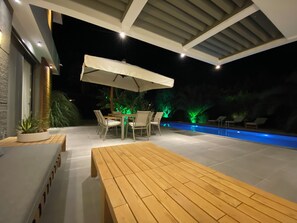 An outdoor patio with a pool, wooden furniture, and a covered seating area.