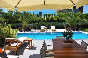 Un área junto a la piscina con sillones, una mesa y una planta en maceta.