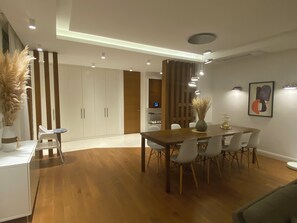 A modern dining area with a wooden table, white chairs, and a vase of dried plants.