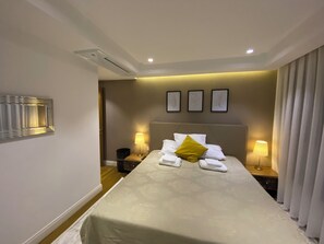A hotel room with a large bed, bedside lamps, a headboard with artwork, and a mirror on the wall.