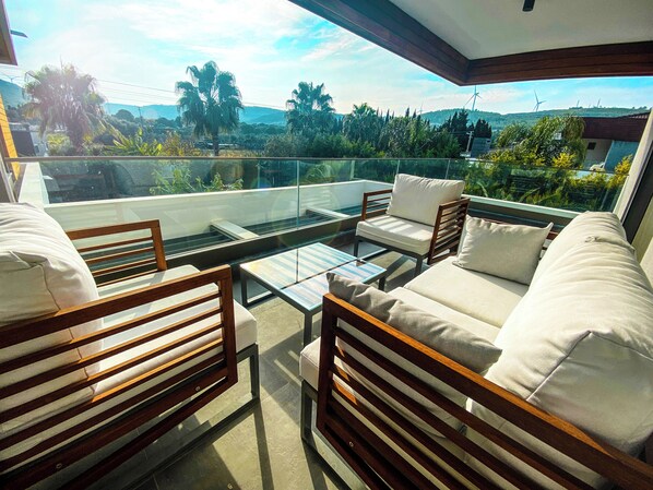 A balcony with a sofa, chairs, and a glass table.