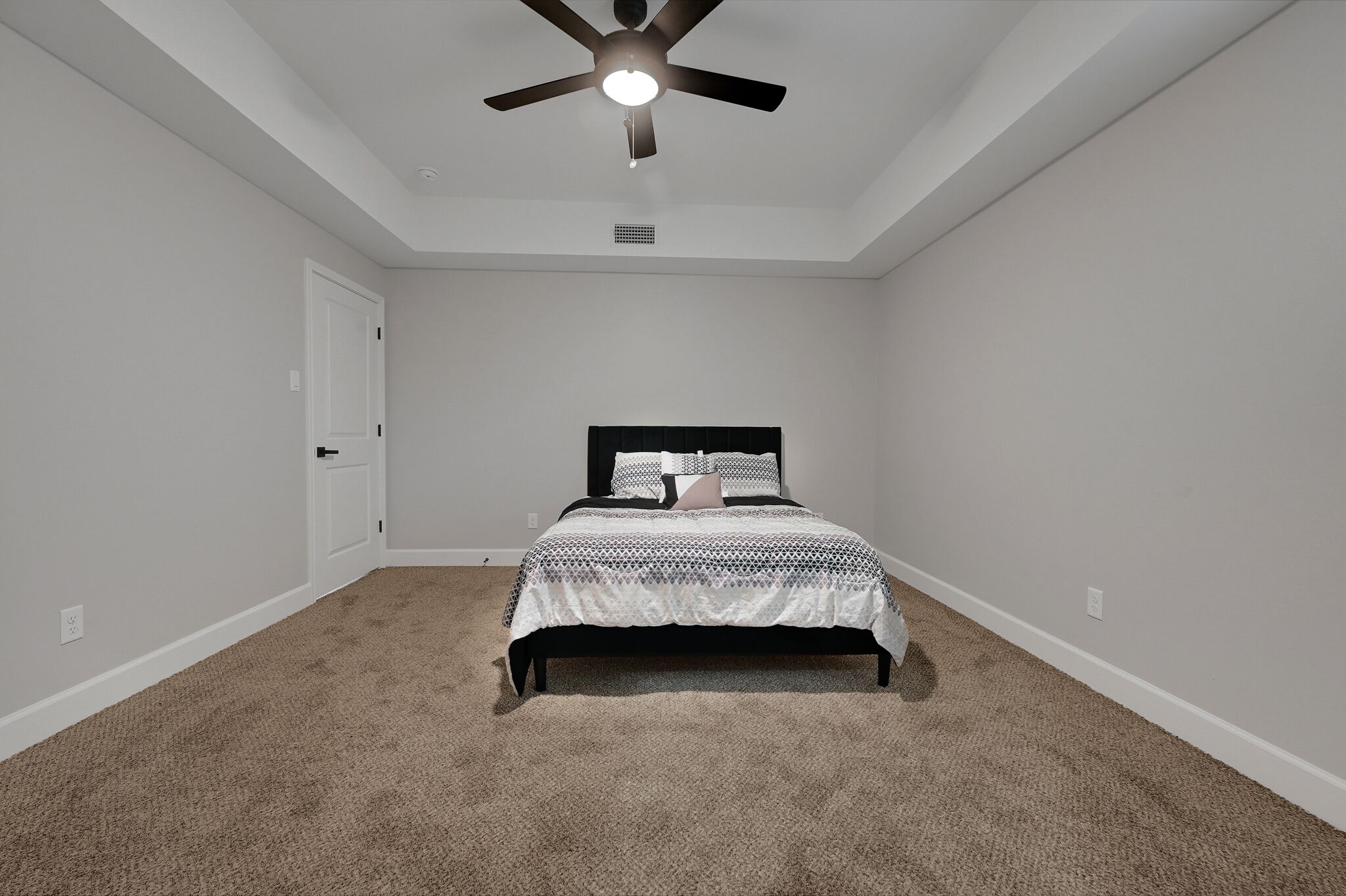 A bedroom with a bed, a ceiling fan, and a door.