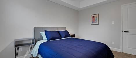 A bedroom with a bed, a bedside table, a nightstand, a ceiling fan, a door, and a wall-mounted artwork.