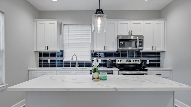A modern kitchen with white cabinets, a central island, a stainless steel microwave, and a built-in oven. - Med Center Luxury stay with free parking!  (Houston)
