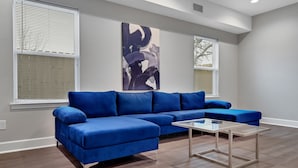 A modern living room with a blue sectional sofa, a glass coffee table, and abstract art on the wall. - Med Center Luxury stay with free parking!  (Houston)
