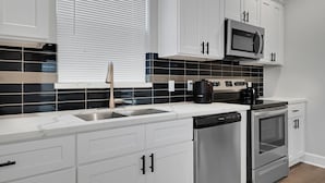 A modern kitchen with white cabinets, a black tiled backsplash, stainless steel appliances, and a window with blinds. - Med Center Luxury stay with free parking!  (Houston)