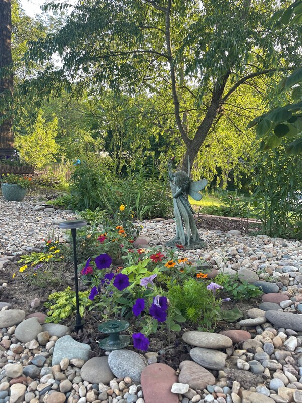 A garden with a statue, pebbles, and various flowers.