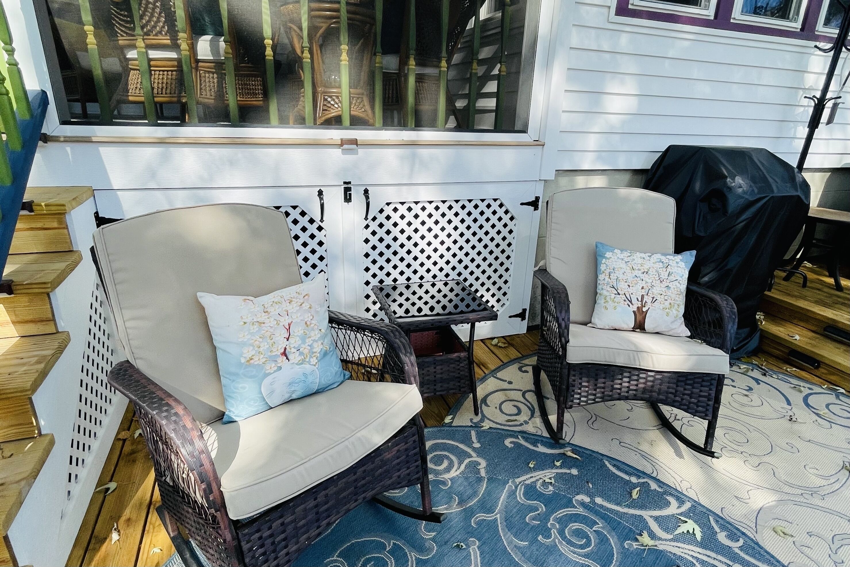 A patio area with wicker chairs and a blue patterned rug.