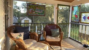 A covered porch with wicker chairs and cushions, a wooden ceiling, and a view of the surrounding trees and a house. - Victorian home brought back to life on the Shawnee Hills wine trail. (Cobden)