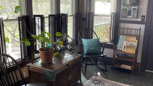 A cozy room with a large window, a wooden table with a plant, a rocking chair, and a patterned rug. - Victorian home brought back to life on the Shawnee Hills wine trail. (Cobden)
