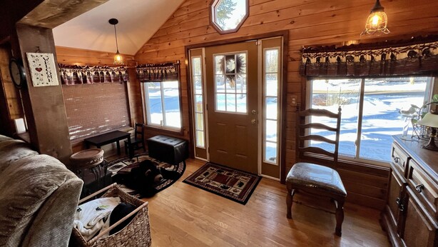 A cozy cabin interior with a wooden ceiling, a bench, a table, and a view of a snowy landscape through the door. - Close to Town, Hot Tub, 2 Kings, 4 Full Beds (Old Forge)