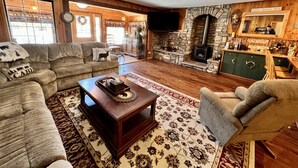 A cozy living room with a stone fireplace, a wooden ceiling, and a television mounted on the wall. - Close to Town, Hot Tub, 2 Kings, 4 Full Beds (Old Forge)