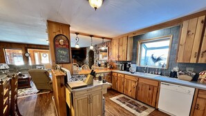 A cozy kitchen with wooden cabinets, a central island, and a stone backsplash. - Close to Town, Hot Tub, 2 Kings, 4 Full Beds (Old Forge)